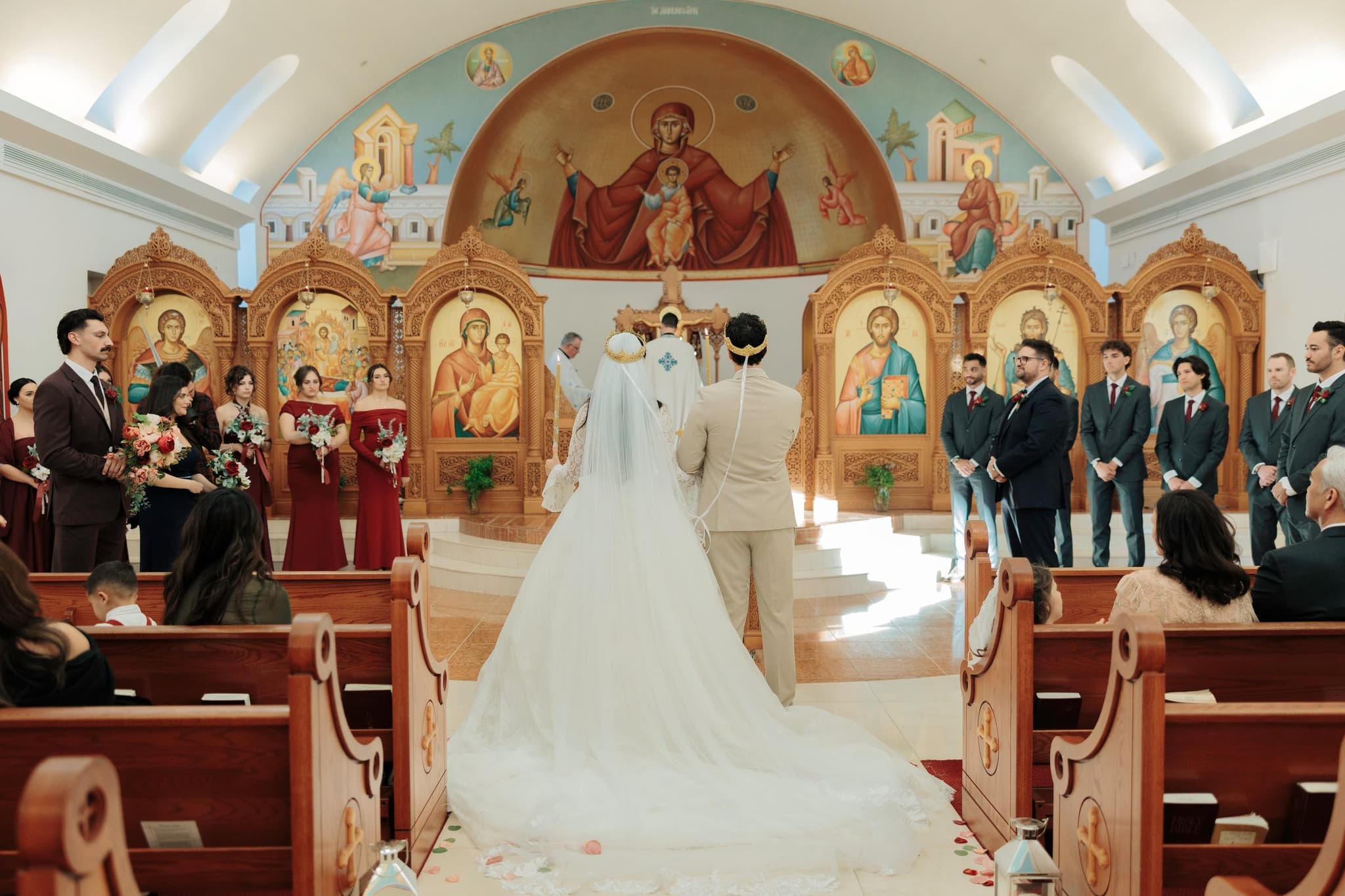 A crowned Orthodox bride and groom stand before the iconostasis during their wedding ceremony